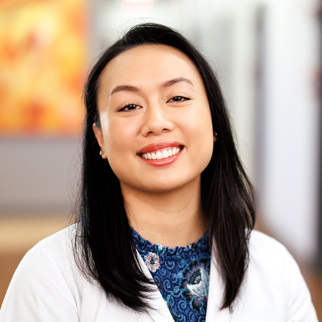 Dr. Dang is standing in the clinic hallway in her white coat and is smiling.