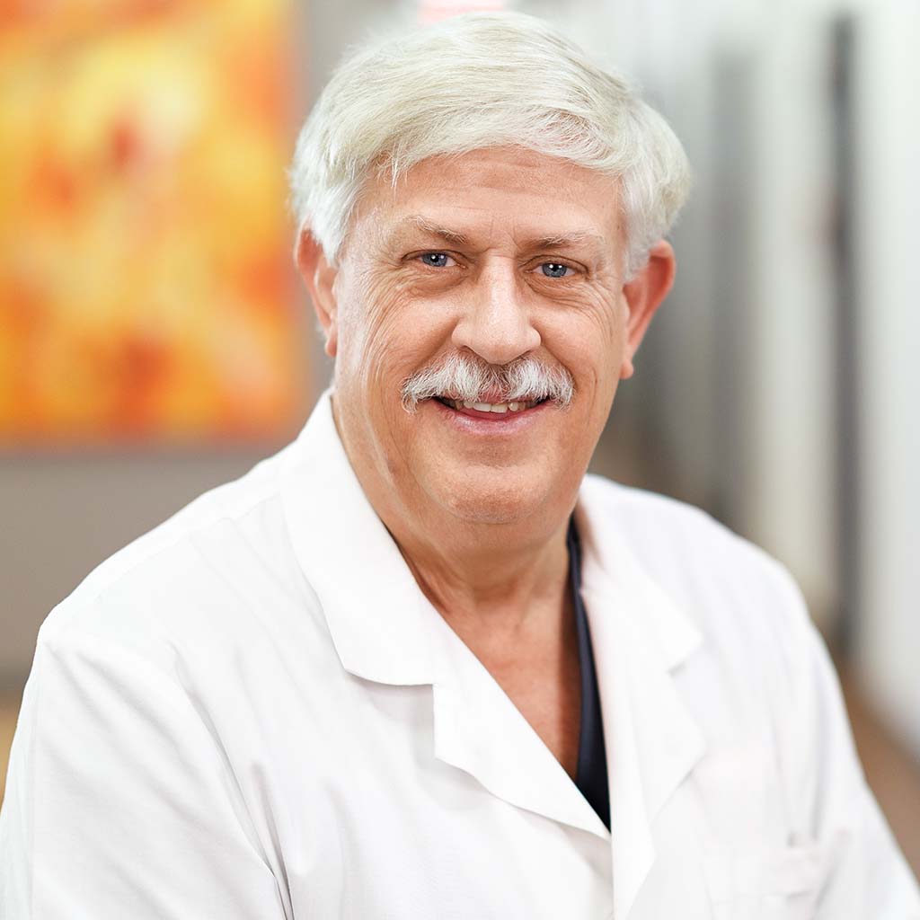 Dr. John Winnie standing in the hallway wearing his white lab coat and smiling at the camera.
