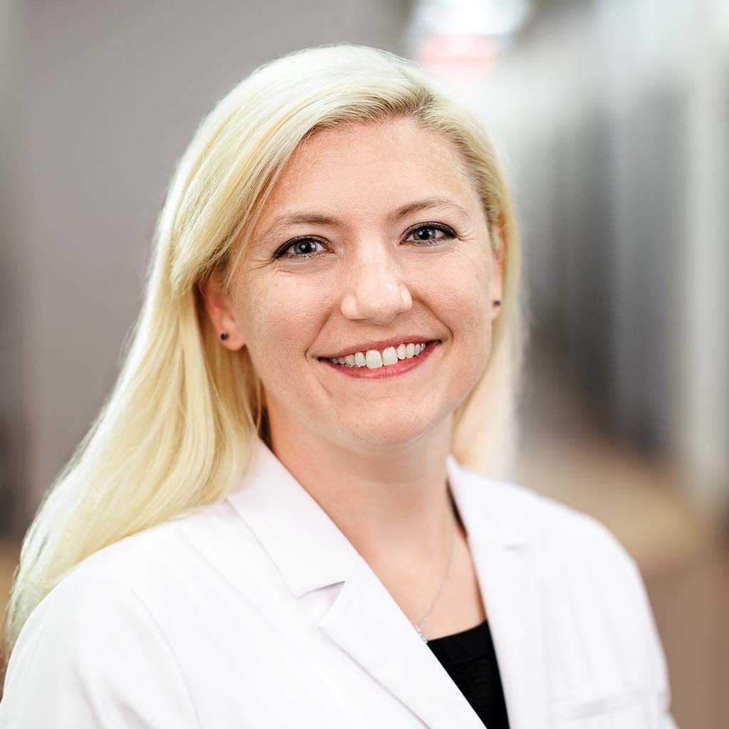 Nurse Practitioner Jana Yates is standing in the clinic hallway and is smiling.